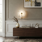 The brushed-brass Clérachic wall sconce glows above a walnut sideboard in a panelled living room.