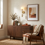 The brushed-brass Clérachic wall light glows beside a walnut sideboard and a framed abstract print.