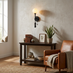 A matte-black Clérachic wall sconce lights a reading corner beside a leather armchair and a potted plant.