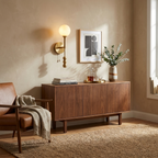 The brushed-brass Clérachic wall light glows above a walnut sideboard set with a framed print and vase.