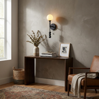 A matte-black Clérachic wall light glows over a console table with a stoneware vase and woven basket.