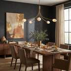 A brushed-brass, five-arm Clérachic chandelier lights a dark charcoal dining room with amber glassware on the table.