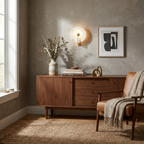 A brushed-brass Clérachic wall light glows over a walnut dresser dressed with a stoneware vase.