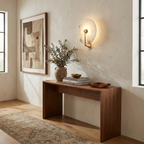 The brushed-brass Clérachic wall light glows over a console table beneath an abstract framed print.