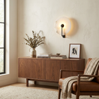 This matte-black Clérachic wall light glows above a walnut sideboard with a stoneware pitcher and books.