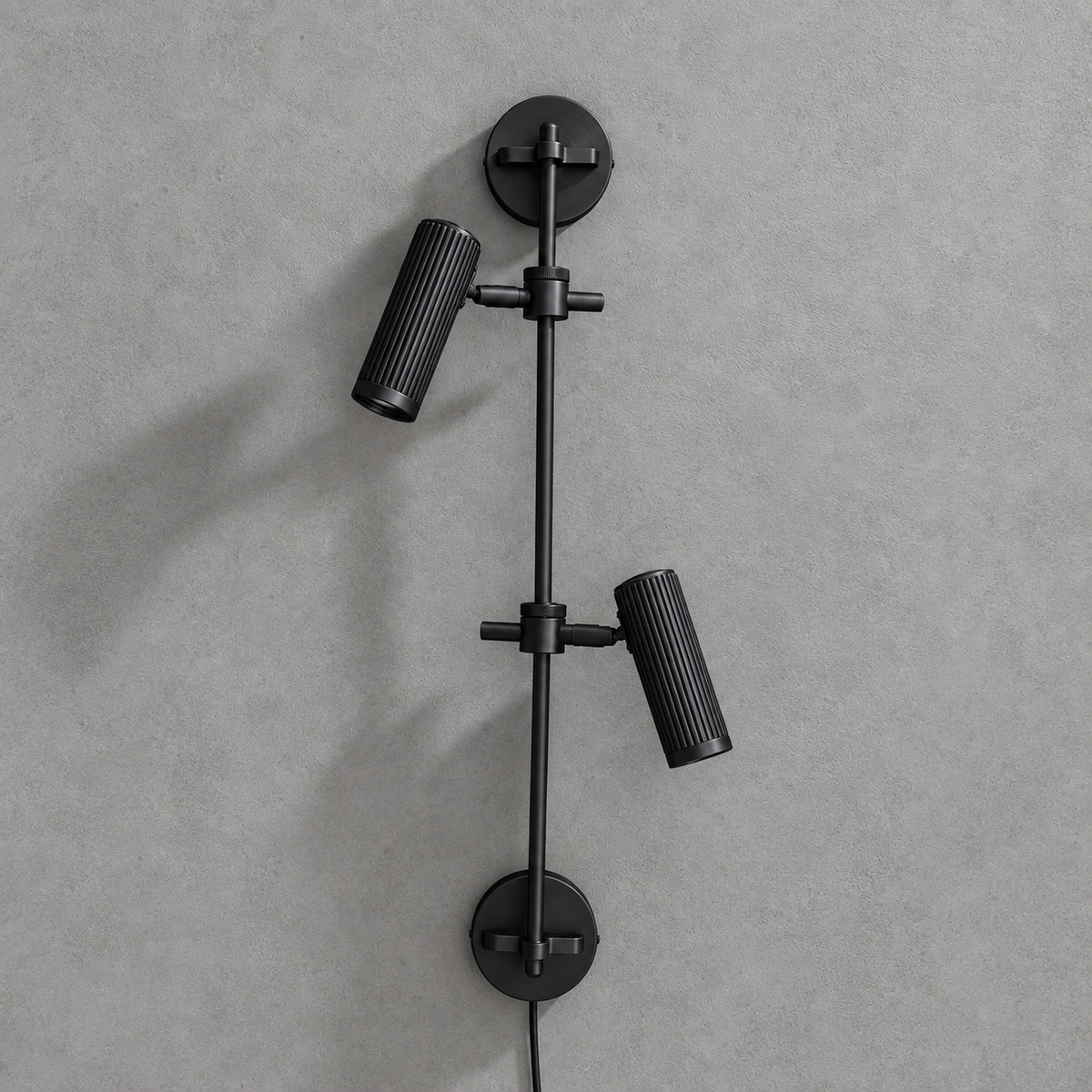 Studio shot of this Clérachic plug-in spotlight in black finish, its two ribbed heads unlit against grey.