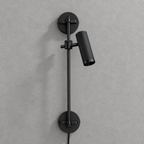 Studio shot of this Clérachic plug-in spotlight in black finish, its cord trailing from the base plate.