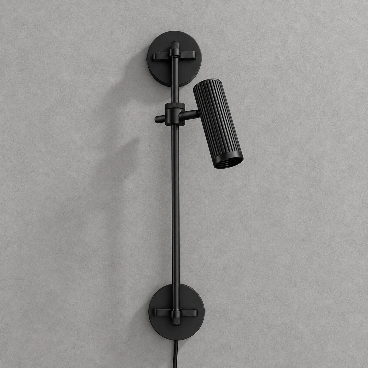 Studio shot of this Clérachic plug-in spotlight in black finish, its cord trailing from the base plate.