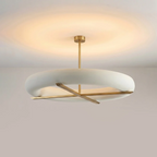 Photographed at an angle, this Clérachic ceiling light's gold cross-frame sits beneath a wide glowing white shade.