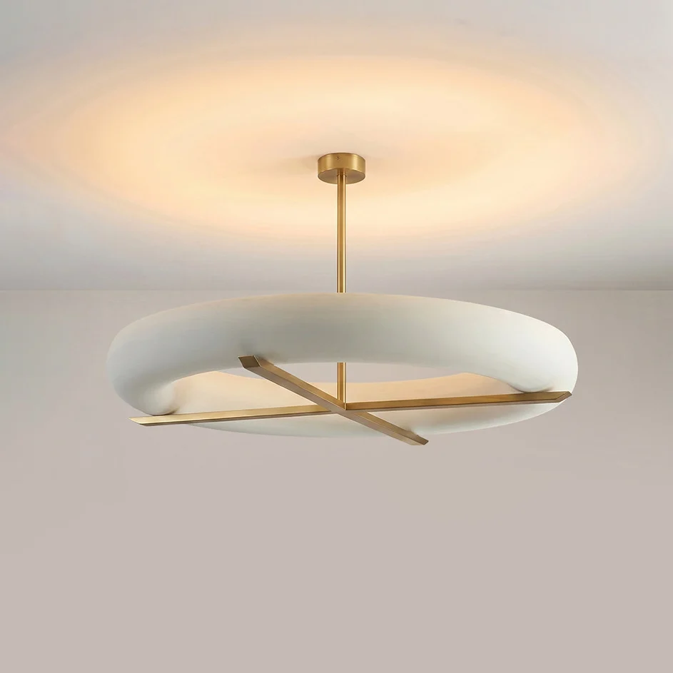 Photographed at an angle, this Clérachic ceiling light's gold cross-frame sits beneath a wide glowing white shade.