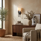 Above a wood sideboard with an olive plant, this Clérachic sconce in black hardware casts a warm glow.