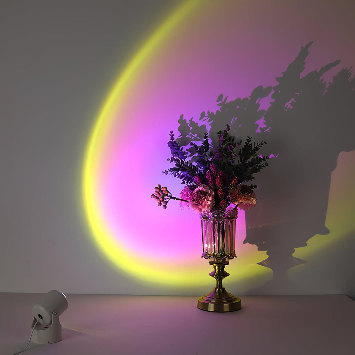 A yellow-green and magenta halo from this Clérachic projection lamp spreads behind a flower-filled vase, its shadow crossing the wall.