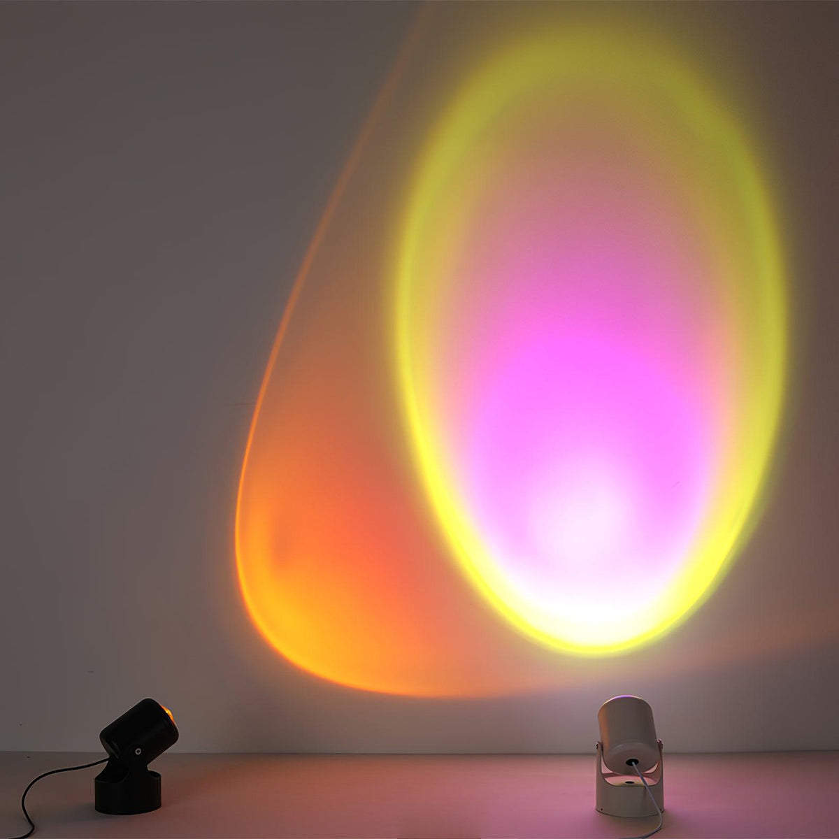Side by side, a black and a white Clérachic projection lamp cast a yellow and magenta gradient halo on a grey wall.