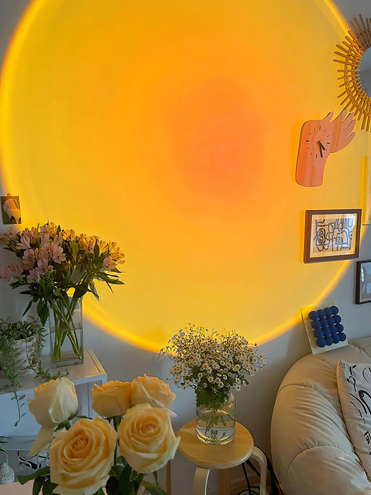 In a cosy living room, this Clérachic projection lamp warms a gallery wall with an orange halo beside framed art and yellow roses.