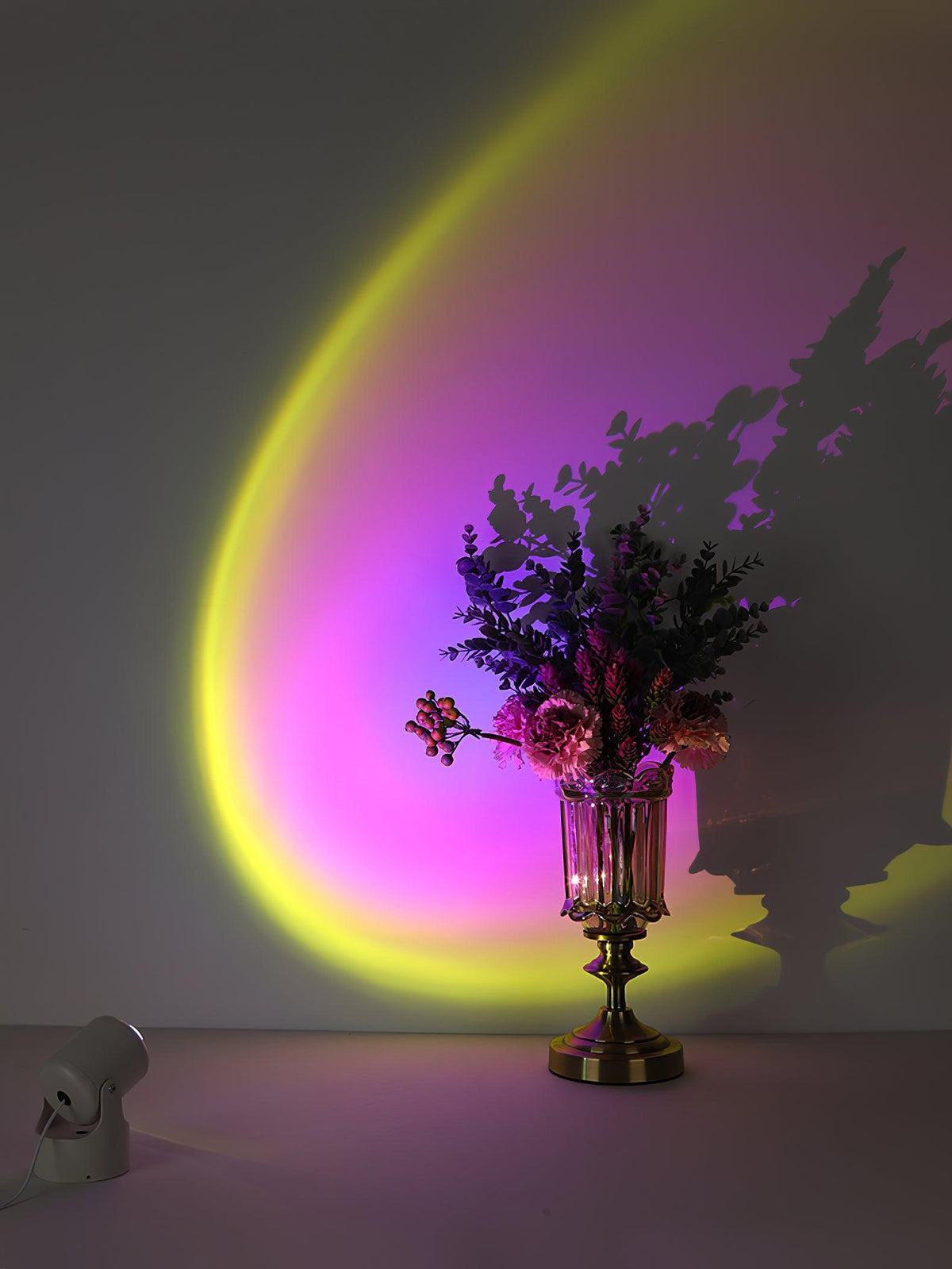 A yellow-to-magenta gradient halo from this Clérachic projection lamp spreads behind a vase of flowers, throwing its shadow on the wall.