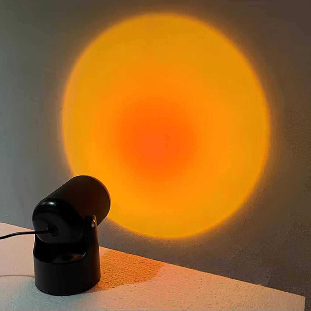 On a tabletop edge, this black Clérachic projection lamp throws a warm orange sunset halo across the wall.