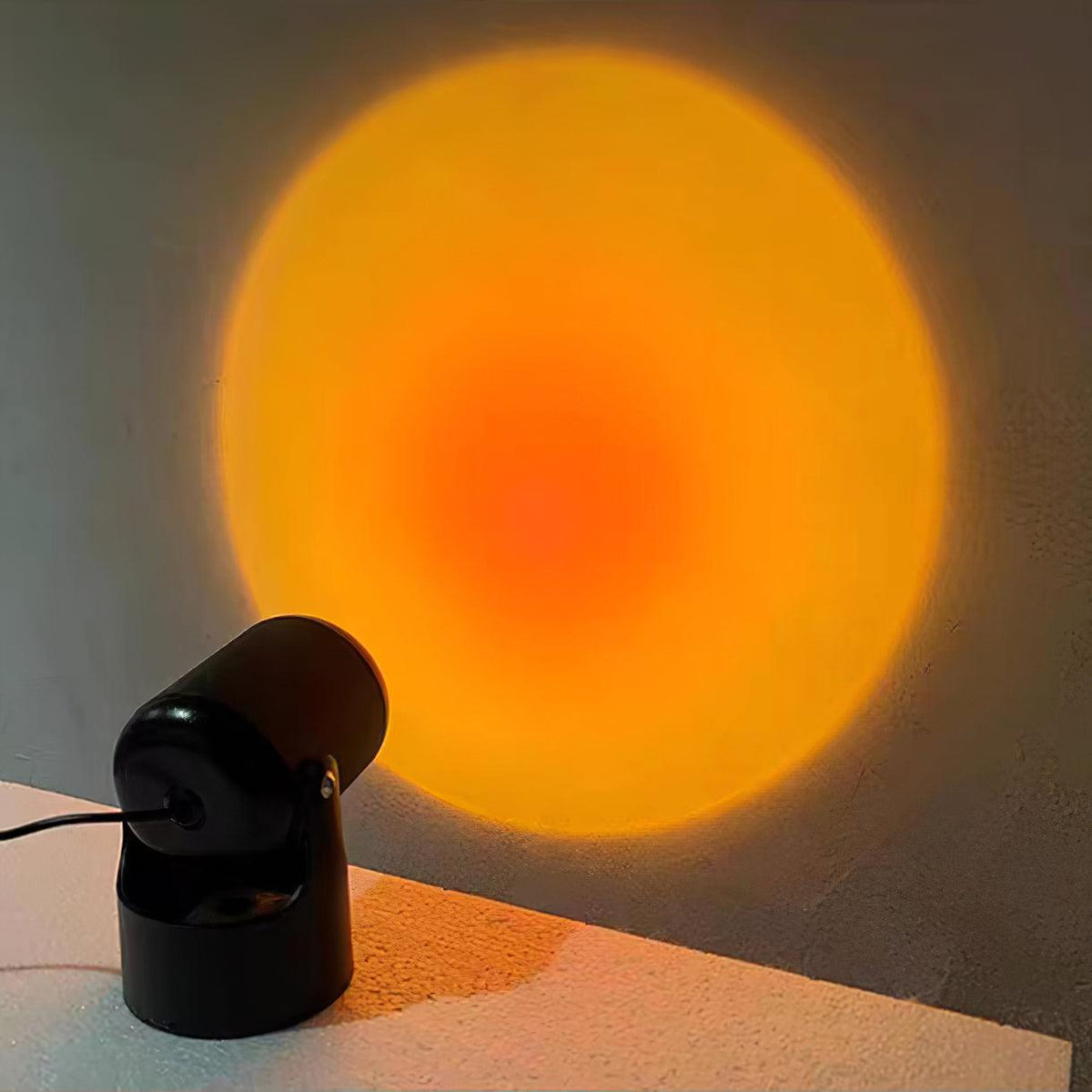 On a tabletop edge, this black Clérachic projection lamp throws a warm orange sunset halo across the wall.
