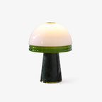 Clérachic table lamp with a glowing white dome shade banded in green glass, set on a dark green marble cone base against a white backdrop.