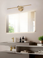 Beside a large mirror, this gold-finish Clérachic wall light glows above a stone-look vanity with folded towels and a small plant.