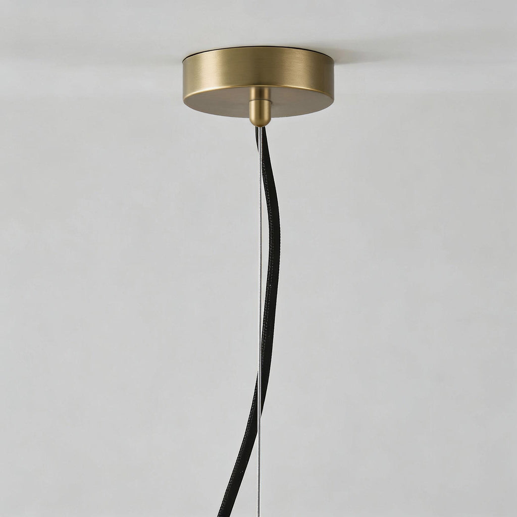 Close-up of the brushed brass ceiling canopy with the black fabric cable and steel suspension wire.
