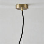 Close-up of the brushed brass ceiling canopy with the black fabric cable and steel suspension wire.