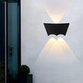 Black wall sconce lit on a white exterior wall beside a glazed door, casting narrow beams up and down.