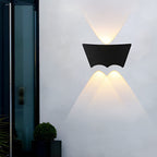 Black wall sconce lit on a white exterior wall beside a glazed door, casting narrow beams up and down.