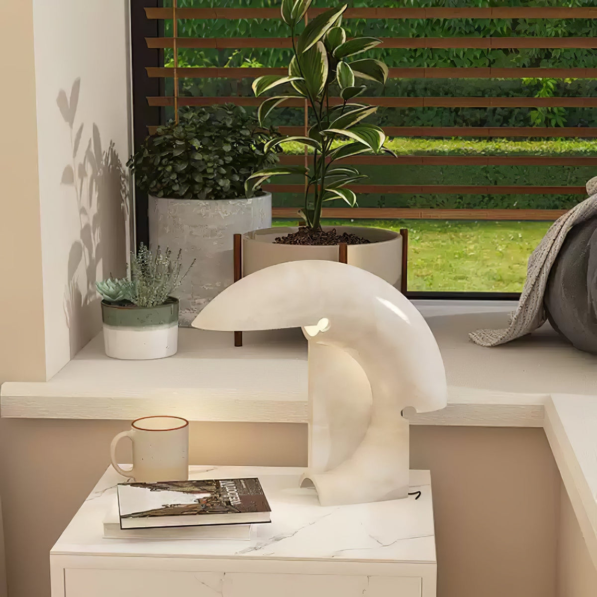 Clérachic resin crescent lamp glowing on a white marble nightstand, with potted plants visible through the window behind it.