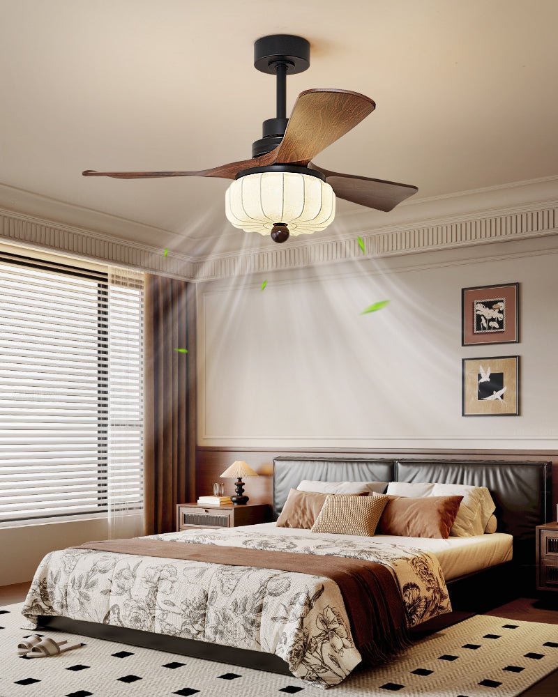 Fitted above a bed with patterned linen and a striped window blind, this Clérachic ceiling fan lights the bedroom with its lantern shade.
