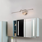 A nickel-finish Clérachic wall light glows above a mirrored bathroom cabinet, mounted on a pale wall.