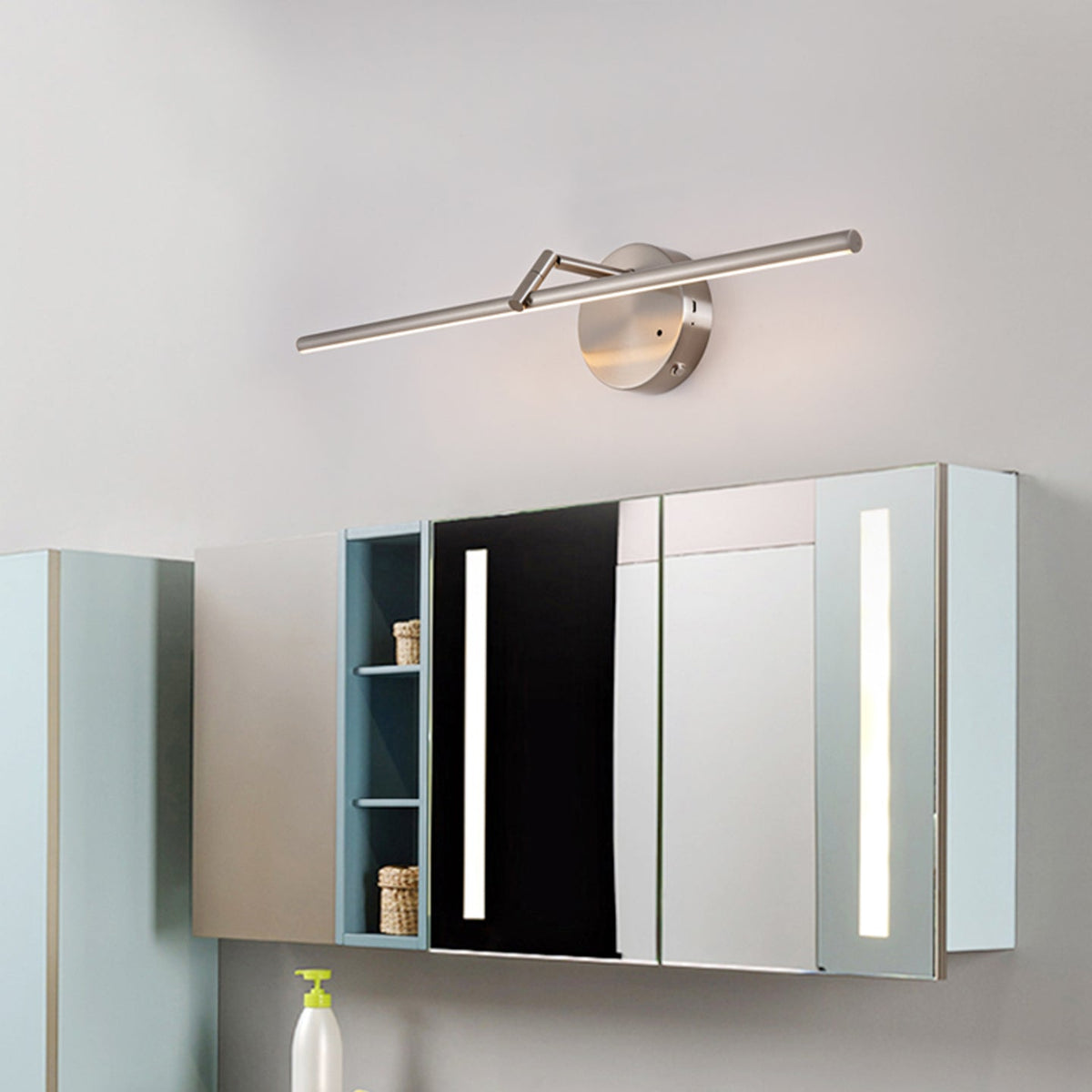A nickel-finish Clérachic wall light glows above a mirrored bathroom cabinet, mounted on a pale wall.