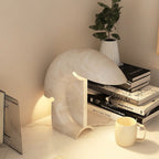 A closer view of the lit Clérachic resin lamp beside stacked books and a small plant, its crescent curve catching the warm light.