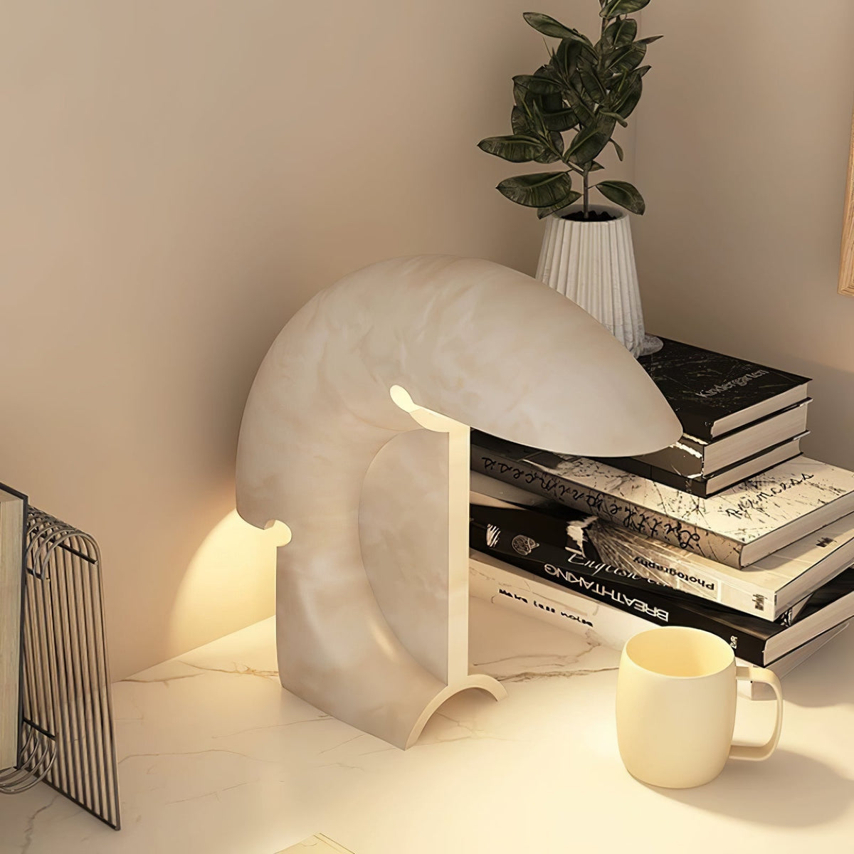 A closer view of the lit Clérachic resin lamp beside stacked books and a small plant, its crescent curve catching the warm light.