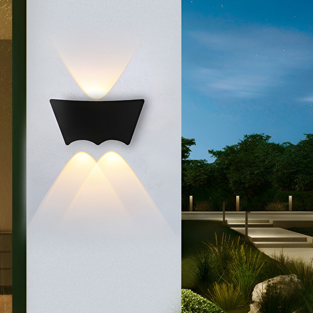 Wall sconce lit on a white pillar at dusk, with a landscaped terrace and lit garden steps beyond.