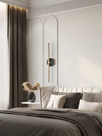 Clérachic wall light fixed beside a neutral bed, its brass bar set against an arched wall panel near soft pillows.