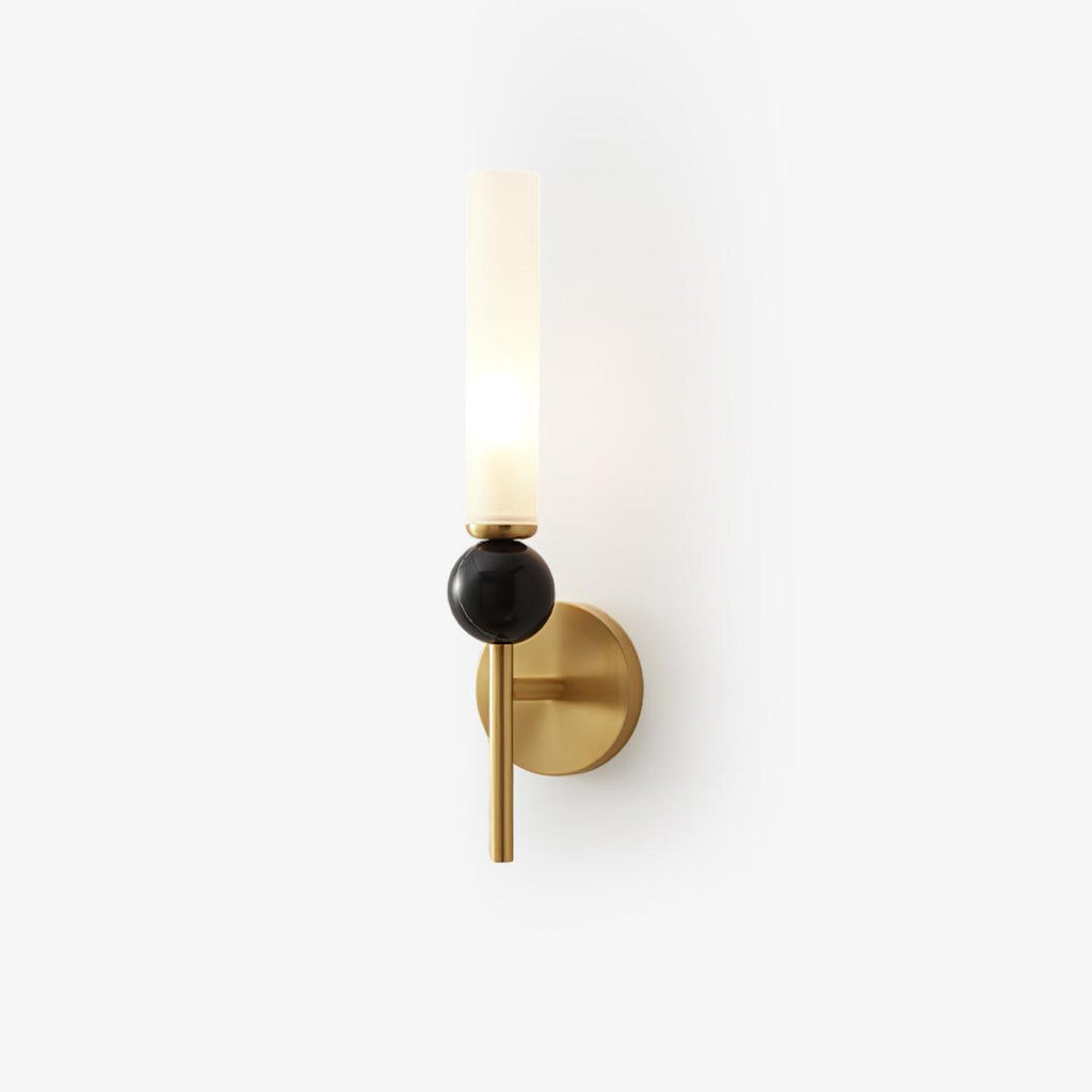 A frosted acrylic tube shade glows above a polished black marble sphere on this Clérachic brass wall sconce, shown alone on white before it hangs in a bedroom.