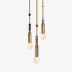 Three Clérachic pendant lights hang at staggered heights, each brass rod strung with different marble beads above a lit bulb.