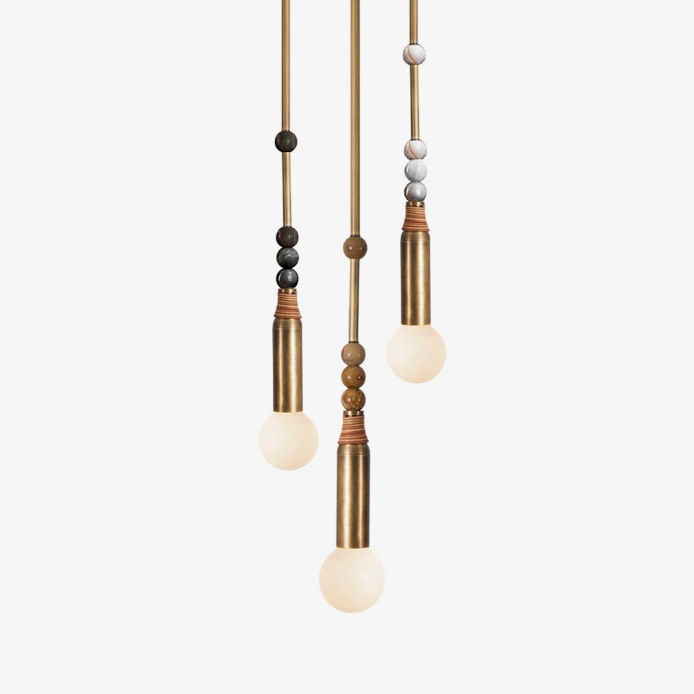 Three Clérachic pendant lights hang at staggered heights, each brass rod strung with different marble beads above a lit bulb.