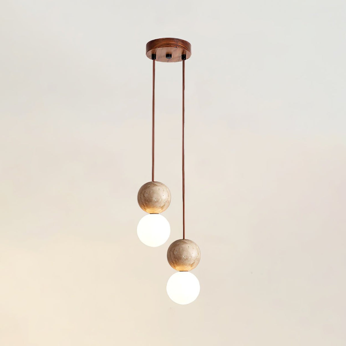 Two cords drop travertine and glass spheres at differing heights from this Clérachic pendant's round canopy, studio shot.