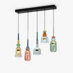 A long black ceiling plate holds five Clérachic pendants in amber, coral, teal, orange-red and sage glass at even height.