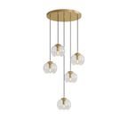 Six small round clear glass shades hang at staggered heights from a gold ceiling plate, this Clérachic fixture shown on white.