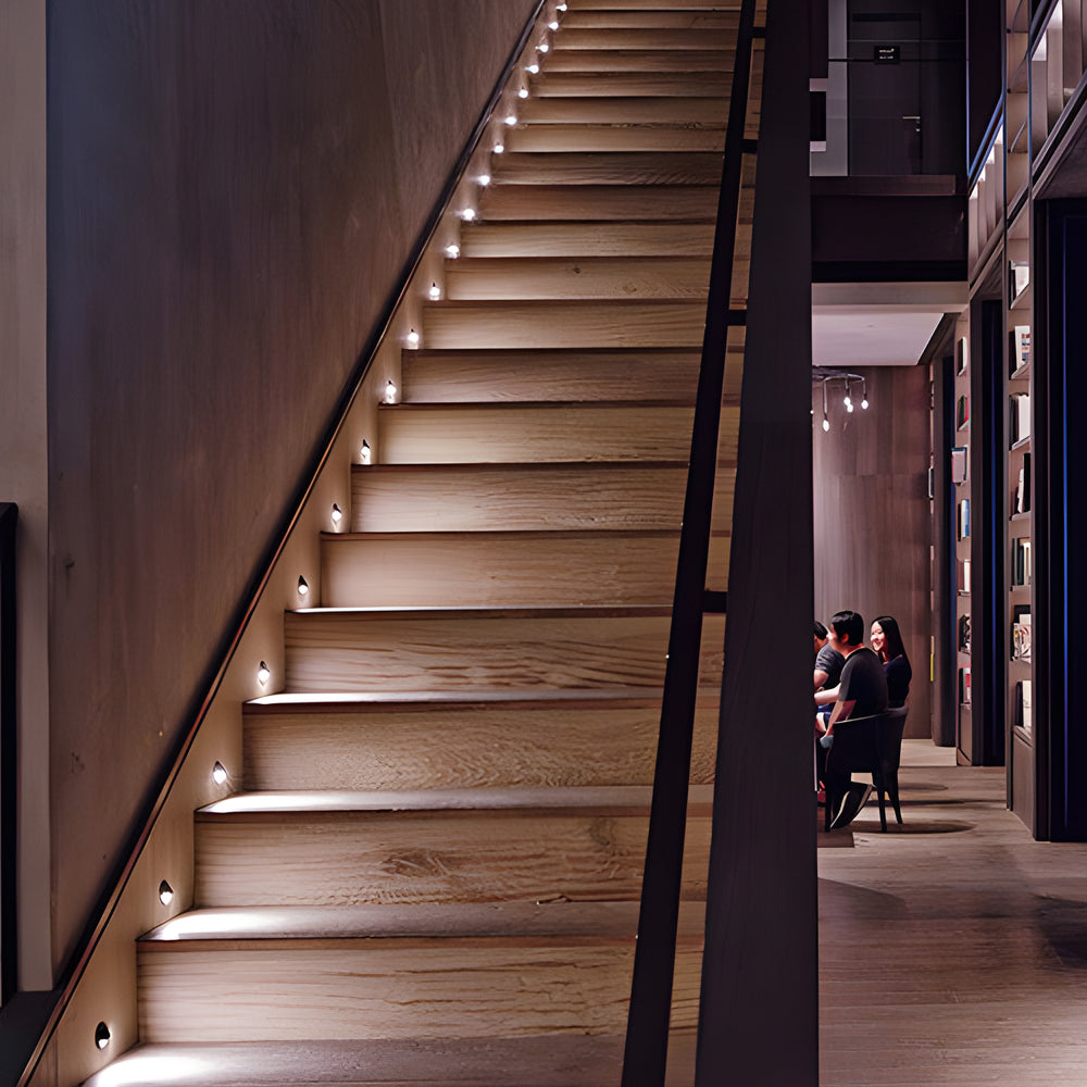 A wooden staircase lit from small round lights recessed into the side wall, treads glowing softly.