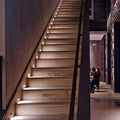A wooden staircase lit from small round lights recessed into the side wall, treads glowing softly.