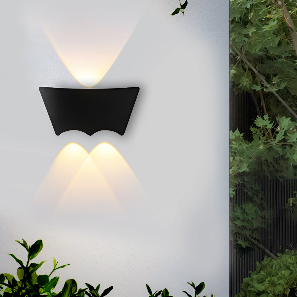 The sconce lit on a garden wall with foliage crowding in at the right, warm light fanning above and below.