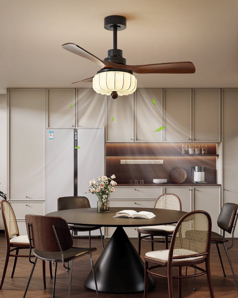 Cane dining chairs circle a round table beneath this Clérachic ceiling fan, its walnut blades and lit lantern shade filling the kitchen corner.