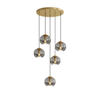Six small round smoky grey glass shades hang at staggered heights from a gold ceiling plate, this Clérachic fixture shown on white.