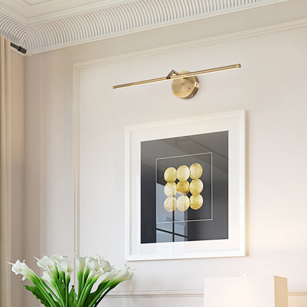 This gold-finish Clérachic wall light glows above a framed black-and-white print, with white flowers and a lamp shade on a console below.