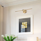 This gold-finish Clérachic wall light glows above a framed black-and-white print, with white flowers and a lamp shade on a console below.