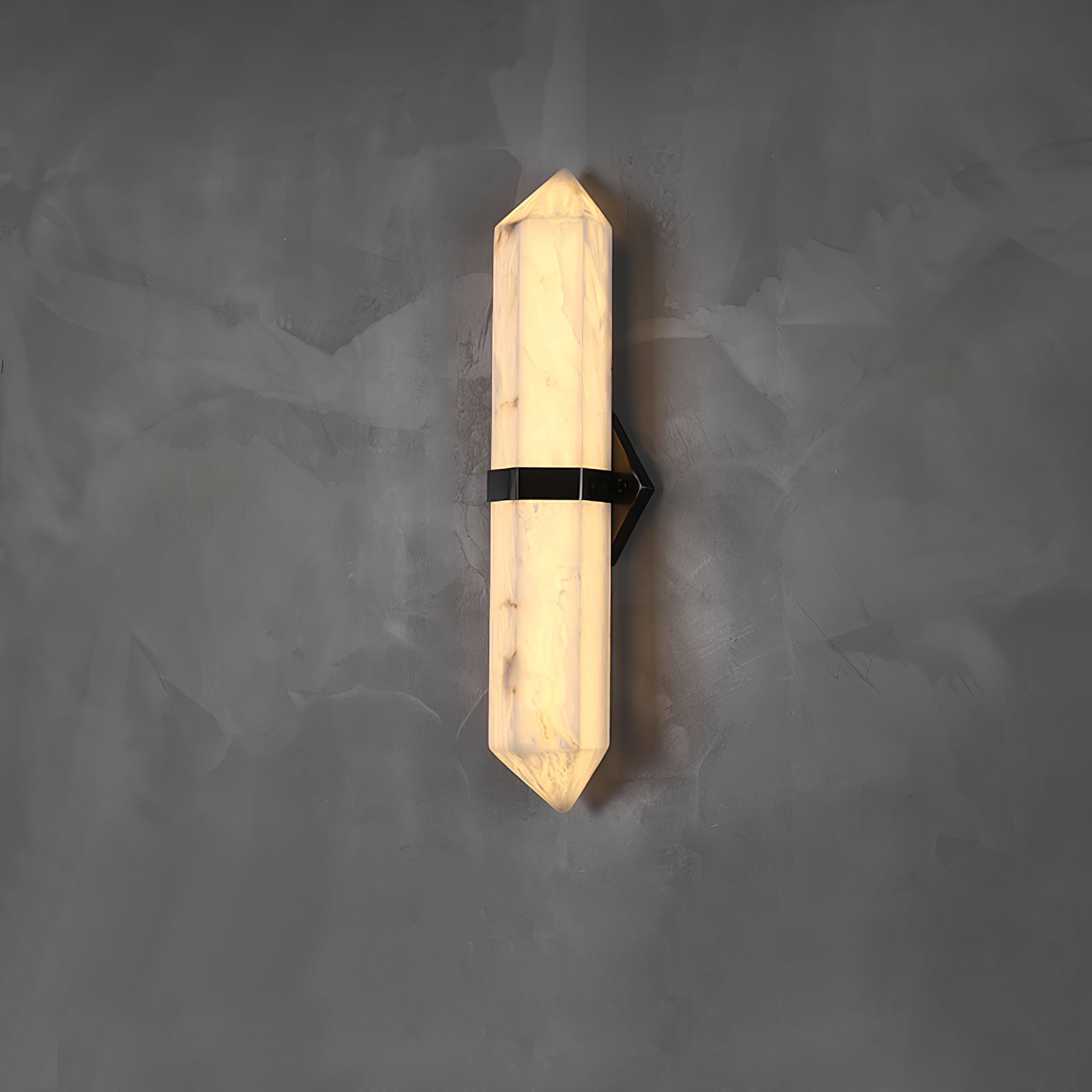 The black-band sconce lit on grey concrete, its pointed tips catching the glow at each end.