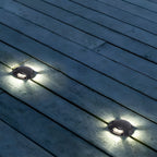 Two deck lights throwing cool white light across grey timber decking at night.